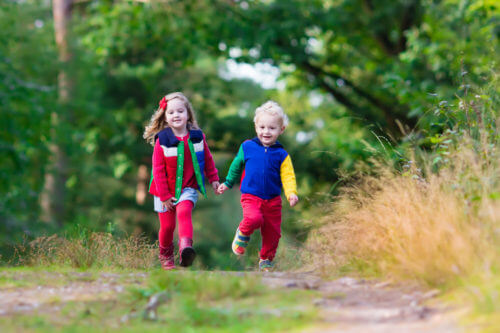 Kids playing in autumn park. Children play outdoors on a sunny fall day. Boy and girl running together hand in hand in a forest. Toddler and preschooler pick colorful oak leaf. Family fun outdoor.